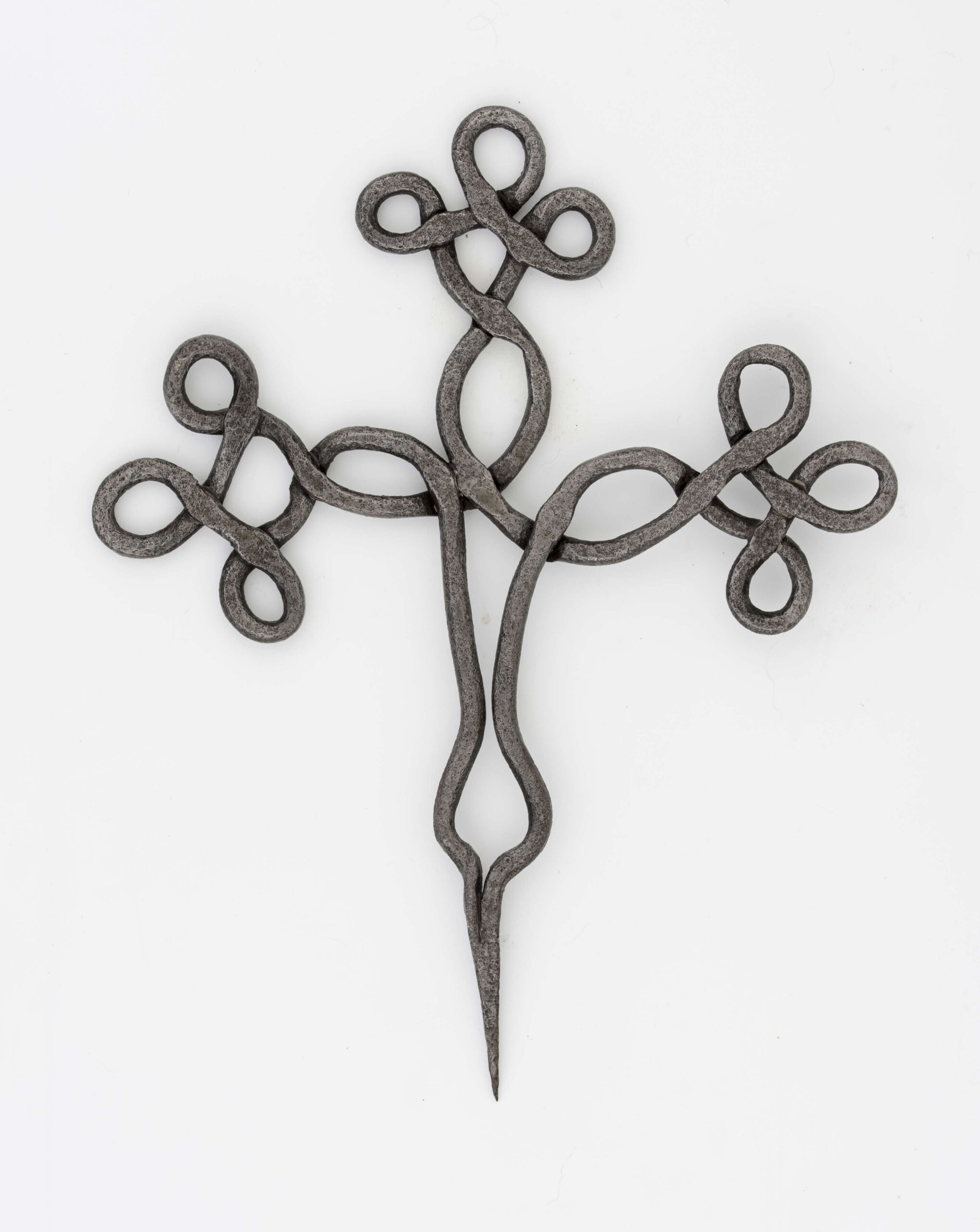 Krzyż żelazny stanowiący zwieńczenie drewnianego krzyża, kowalskiej roboty. Wykonany z pręta o śred. 0,7 cm. Ramiona i wierzchołek krzyża ozdobnie plecione. Szpikulec dł. 6,5 cm.