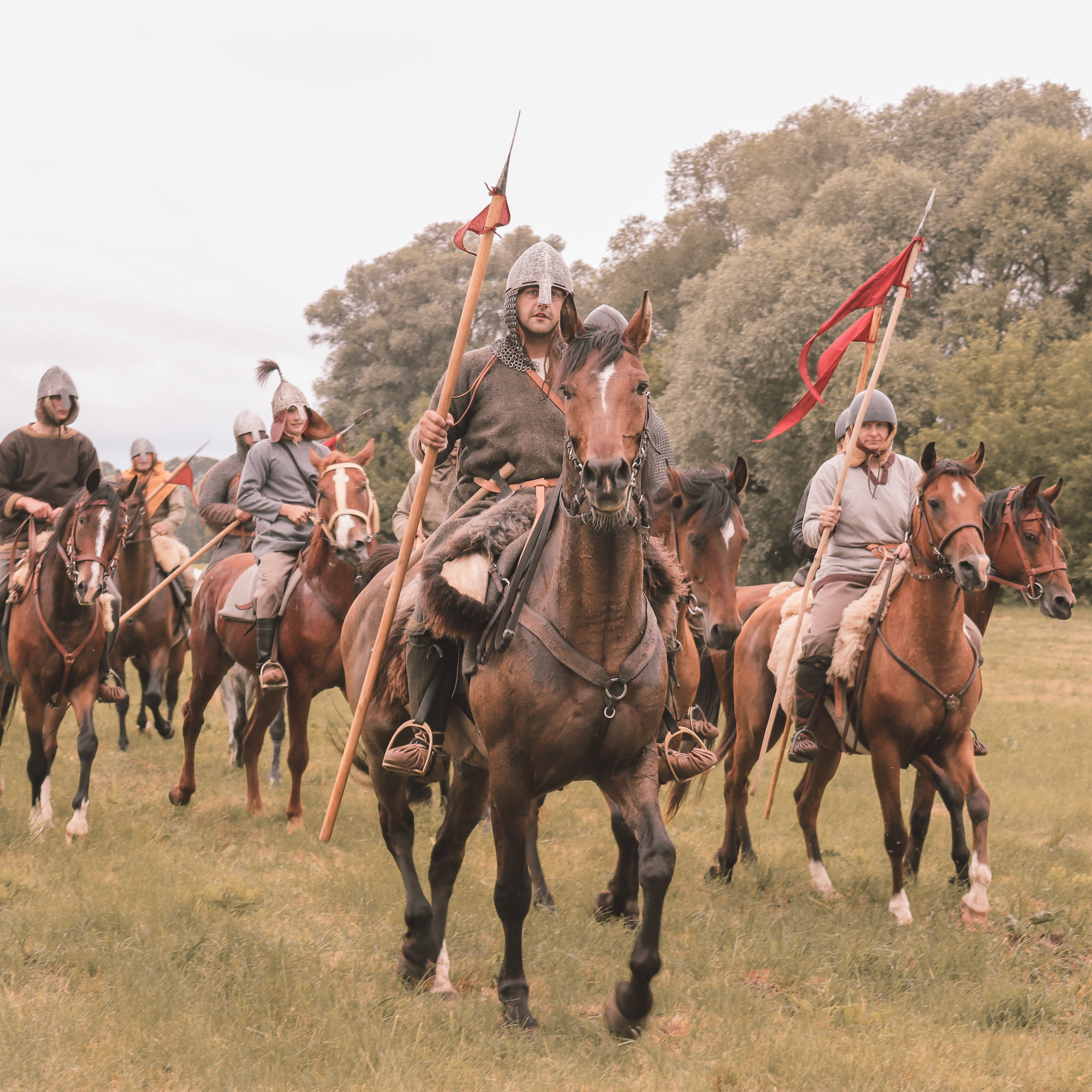 Kilku mężczyzn przebranych za rycerzy średniowiecznych jedzie na koniach.