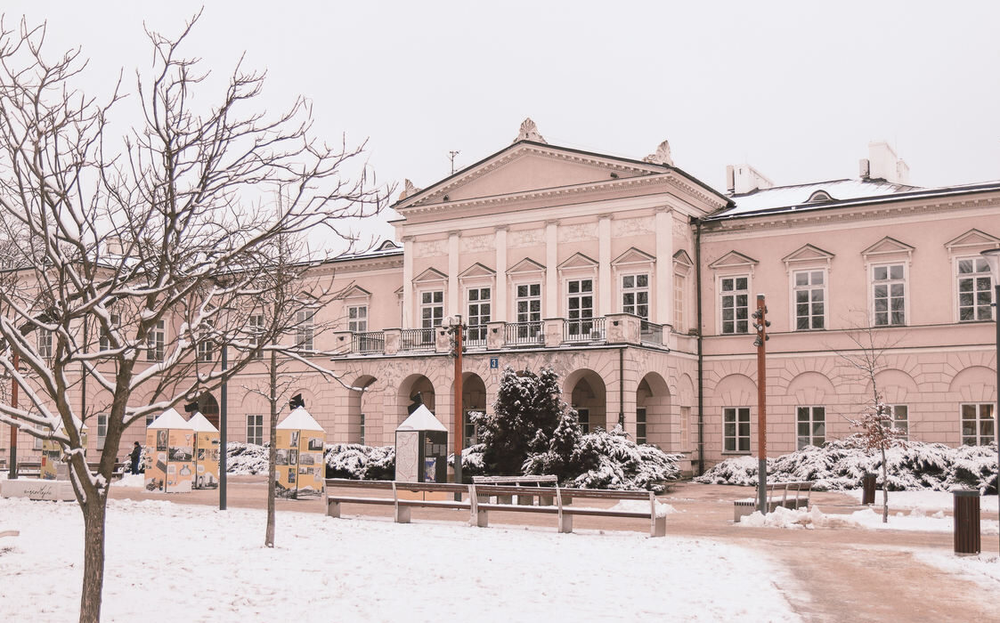 W centrum klasycystyczny budynek Pałacu Lubomirskich. Na pierwszym planie z lewej strony drzewko bez liści. Wszystko przykryte jest śniegiem.