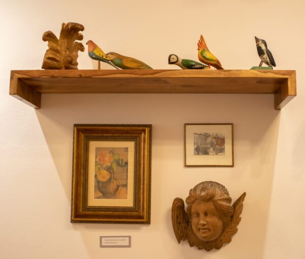 półka na ścianie, na niej figórki etnograficzne przedstawiające ptaki pod spodem obrazy, głowa aniołka