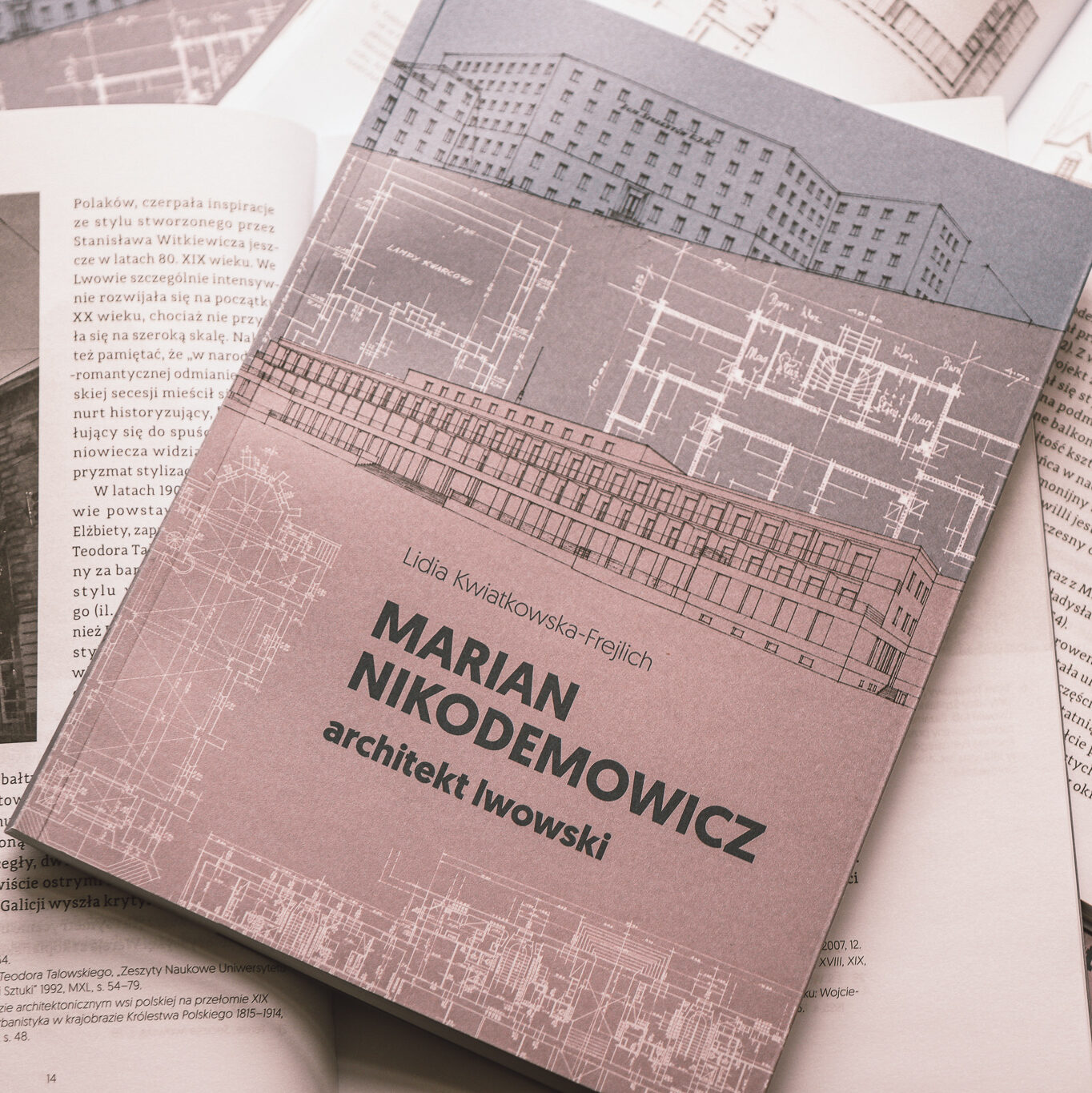 W centrum zdjęcia leży książka pod tytułem Marian Nikodemowicz architekt lwowski. Znajduje się ona na innych książkach, które są otwarte.