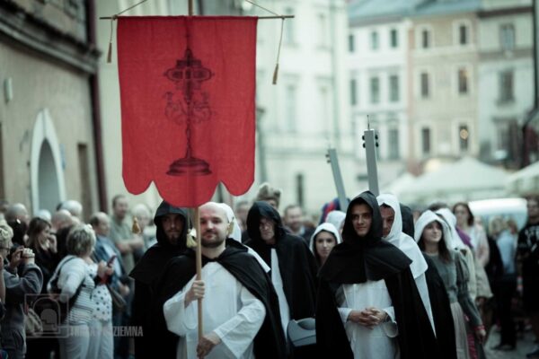 Garfika przedstawiająca korowód dominikanów. Na pierwszym planie zakonnik w białym habicie i czarnej pelerynie niesie chorągiew w kolorze czerwonym. Za nim tłum ludzi.