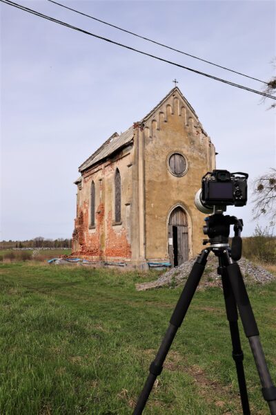 Zdjęcie neoromańskiego kościółka, na pierwszym planie kamera na statywie